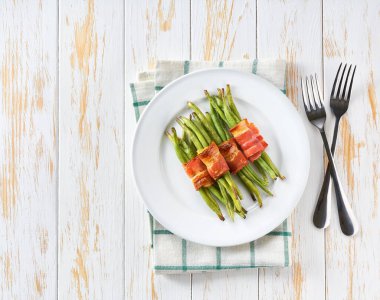 Kavrulmuş pastırma dilimlerine sarılmış fasulyeler beyaz ahşap bir masada seramik bir tabakta, üst tarafta..