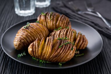 Geleneksel pişmiş Hasselback patatesi ahşap bir masada siyah bir tabakta..