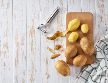 Beyaz ahşap bir masada soyulmuş organik patatesler..