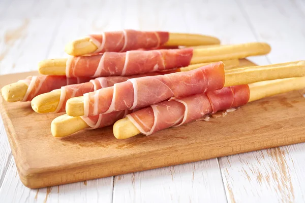 stock image Parma ham prosciutto with Italian grissini breadsticks on a white wooden table .