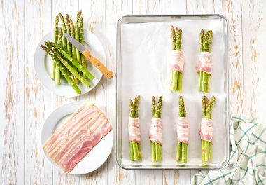 Aperatif pişirmeye hazır, ahşap masadaki bir tepside domuz pastırmasına sarılı yeşil kuşkonmaz. Adım adım tarif et. Sıcak meze tarifleri. Şükran Günü.