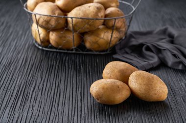 Patates yığını, arka planda patates metal sepetli, siyah ahşap bir masanın üzerinde..