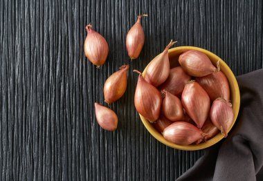 Siyah masa manzaralı ahşap tabakta soğan soğanı. Tahta bir kasede soğan soğanları siyah tahta bir masanın üstünde, üst tarafta..