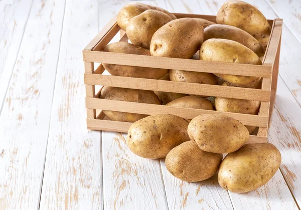 白いキッチンテーブルの上の木製の箱の中の生の黄色のジャガイモ — ストック写真