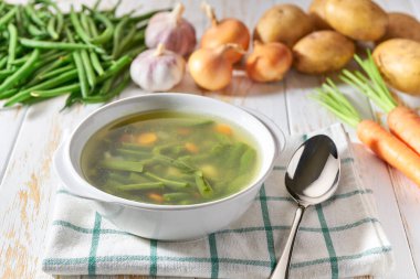 Patatesli yeşil çorba, yeşil fasulye ve ahşap arka planda beyaz bir tabakta havuç..