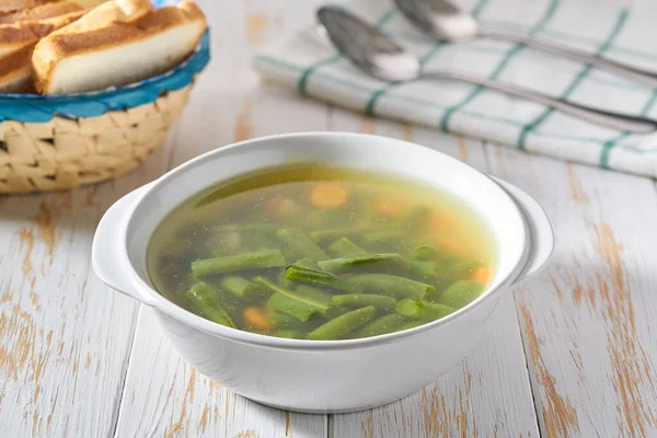 Green soup with potato, green bean and carrot on a white plate on wooden background.