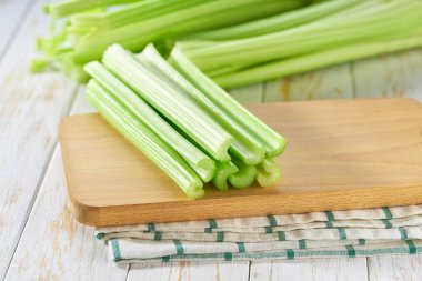 Taze yeşil kereviz sapları beyaz ahşap bir masada.