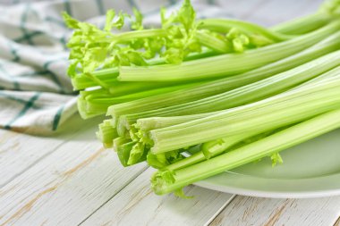 Taze yeşil kereviz sapları beyaz ahşap bir masada.