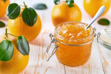 Cam kavanoz portakal reçeli ve beyaz ahşap masa üzerinde taze portakallar..