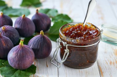 Cam kavanoz incir reçeli ve beyaz ahşap bir masada taze incir..