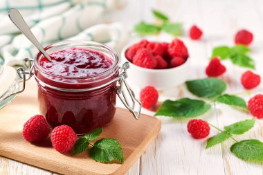 Ev yapımı reçel. Beyaz ahşap bir masada cam bir kavanoz ahududu reçeli. Ev yapımı ahududu reçeli, taze böğürtlen ve mutfak masasında yeşil yaprak..