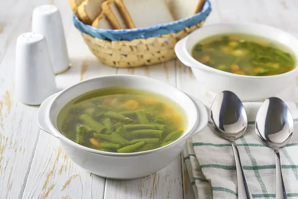 Delicious vegetable soup with green beans, potato, and carrot on a white wooden table.