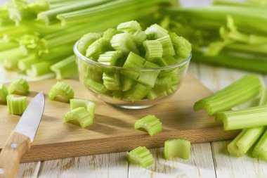 Beyaz ahşap arka planda bir kasede taze dilimlenmiş kereviz, seçici bir odak..