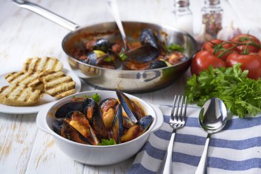 Kızartma tavasında domates soslu kızarmış midye, beyaz bir masada, üst tarafta..