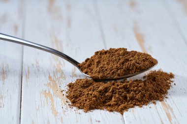 Beyaz tahta bir masada metal kaşıkta tarçın tozu, seçici bir odak..