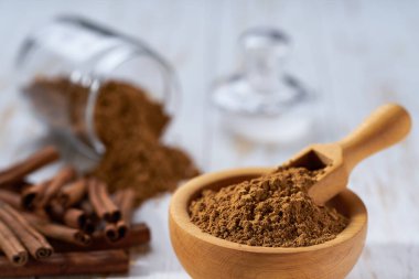 Tarçın çubukları ve ahşap kase beyaz ahşap bir masa üzerinde tarçın tozu, seçici odak.