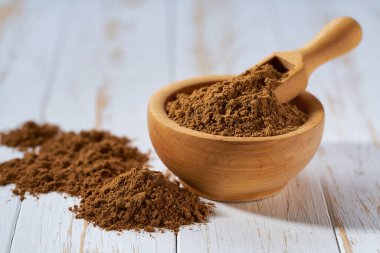 Tahta bir kasedeki tarçın tozu beyaz ahşap bir masada, seçici bir odak.