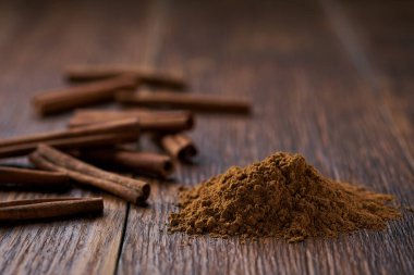 Tarçın çubukları ve tarçın tozu koyu ahşap bir masada..