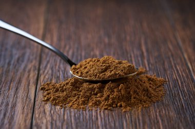 Koyu ahşap bir masada metal kaşıkta tarçın tozu, seçici bir odak.