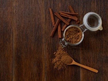 Tarçın çubukları ve tarçın tozu. Koyu ahşap bir masa, üst manzara..