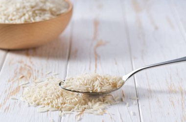 Beyaz ahşap bir masa üzerinde uzun pirinç basmati ile metal kaşık.