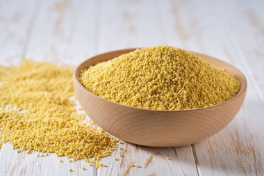 Çiğ darı sarı taneleri ahşap kaseden yayılmış, seçici bir odak noktası var..