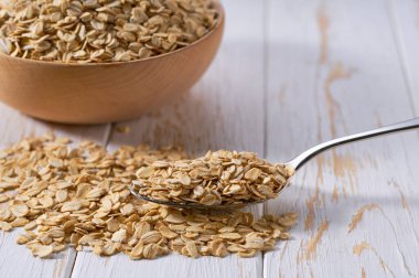 Beyaz ahşap bir masada organik kuru yulaf ezmeli metal kaşık..