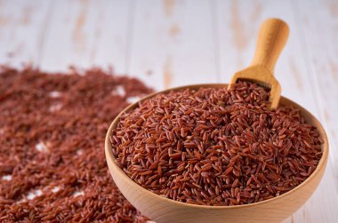 Organik kırmızı pirinç, ahşap kaseden seçici bir şekilde seçilmiş bir masanın üzerine serpilmiştir..