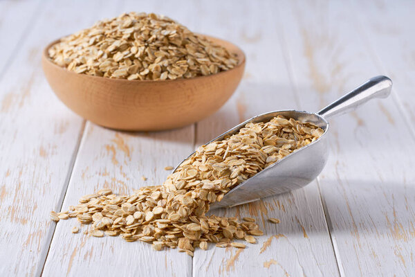 Органический сухой овес вытекает из металлического совок на легкий стол, избирательный фокус.