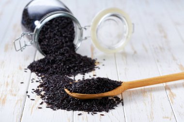 Tahta kepçe içinde organik pirinç taneleri ve cam saklama kavanozunda seçici bir odak noktası var..