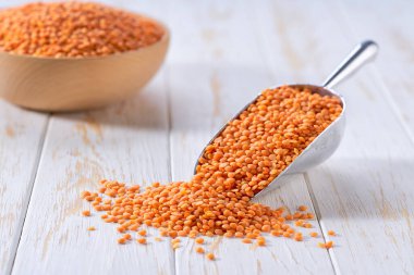 Kırmızı organik mercimekler, seçici bir odak noktası olan hafif bir masanın üzerindeki metal kepçeden dökülür..