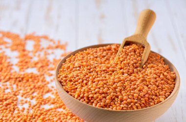 Organik kırmızı mercimekler ahşap kaseden seçici bir şekilde seçilmiş bir masanın üzerine serpilmiştir..