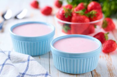 Seramik bir kasede pembe smoothie beyaz bir masada taze çilek, seçici bir odak.