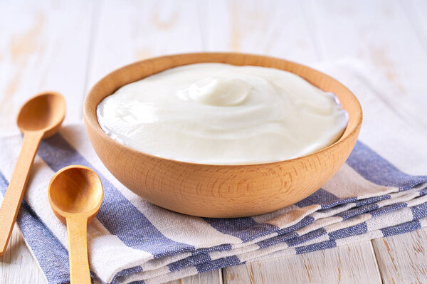 greek yogurt in a wooden bowl with spoon on a white table, selective focus.