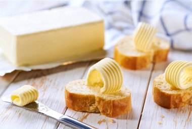 Tahta bir masada ekmek diliminde tereyağlı bukleler, seçici bir odak. Tahta bir masada taze tereyağlı lezzetli baget ekmeği..