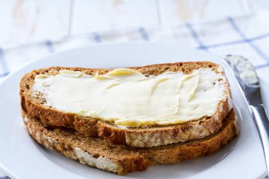 Tahta bir masanın üzerinde tereyağlı çoklu tahıllı ekşi ekmek dilimleri..