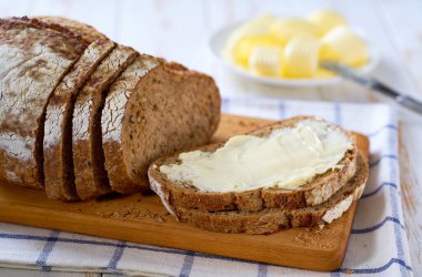 Beyaz ahşap bir masada taze tereyağlı çoklu tahıllı ekşi ekmek..