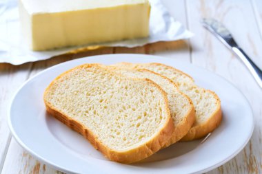 Buğday ekmeği ve tereyağı, beyaz ahşap bir masanın üzerinde, seçici bir odak noktası..