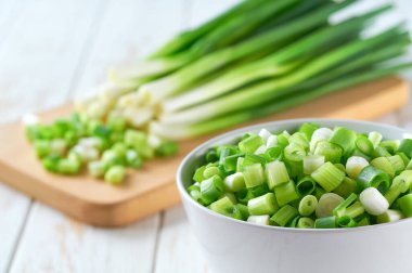 Beyaz bir masada, seramik bir kasede taze yeşil soğan ya da soğan doğranmış..