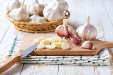 Kesme tahtasındaki organik sarımsak ve soğanlar, arka planda soyulmamış bir yığın sarımsak..