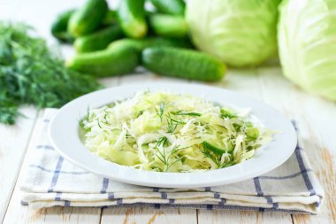 Beyaz ahşap bir masada lahana, salatalık ve dereotlu bahar vejetaryen salatası..