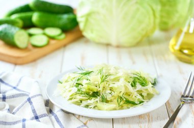 Beyaz ahşap bir masada ev yapımı lahana, salatalık ve dereotu salatası, seçici bir odak noktası. Vejetaryen ya da diyet.