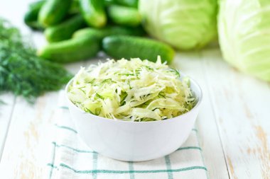 Beyaz ahşap bir masada ev yapımı lahana salatası, salatalık ve dereotu..