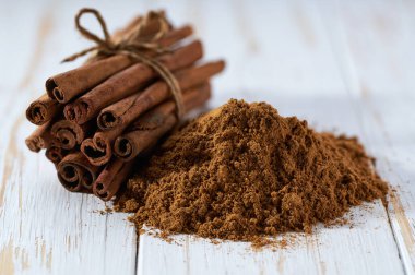 Tarçın çubukları ve tarçın tozu beyaz ahşap bir masa üzerinde, seçici bir odak.