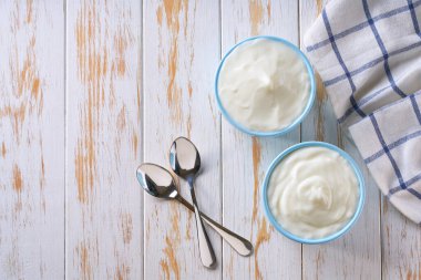 Mavi bir seramik kasede beyaz bir masanın üstünde kaşık ve peçete bulunan doğal yoğurt. Yoğurt konseptinden sağlıklı yiyecekler.