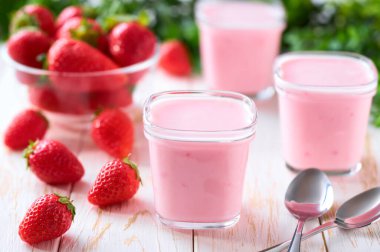 Cam kavanozlarda ev yapımı çilekli smoothie beyaz bir masada taze çilek, seçici bir odak.