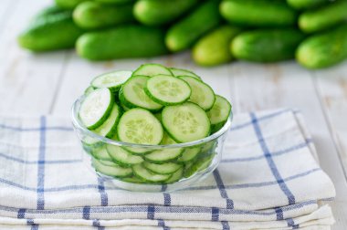 Salatalıklar, tahta bir masada, cam bir kasede, seçici bir odak noktası olan organik salatalıklar..