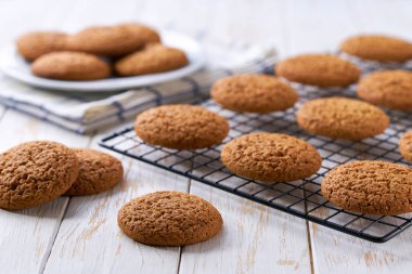 Taze pişmiş yulaflı kurabiyeler siyah tel askıda soğutuluyor, açık mutfak masasında, seçici bir odak noktası var..