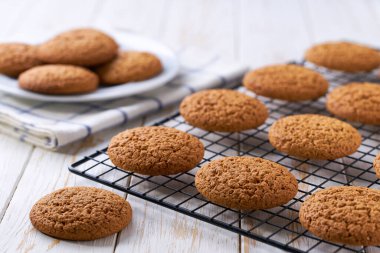 Taze pişmiş yulaflı kurabiyeler siyah tel askıda soğutuluyor, açık mutfak masasında, seçici bir odak noktası var..