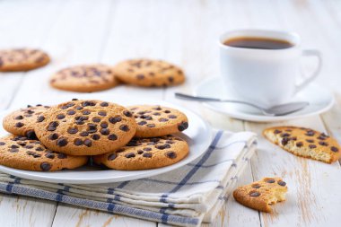 Çikolata parçalı lezzetli kurabiyeler ve açık mutfak masasında kahve, seçici bir odak..